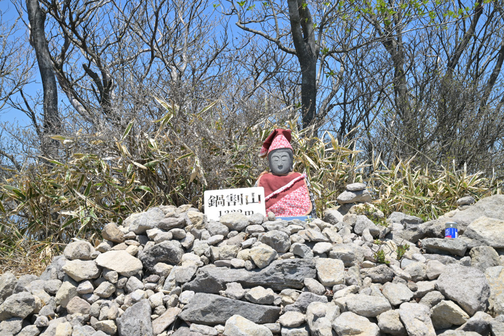 鍋割山の山頂に静かに佇むお地蔵さんの石像と、その背後に広がる開けた景色