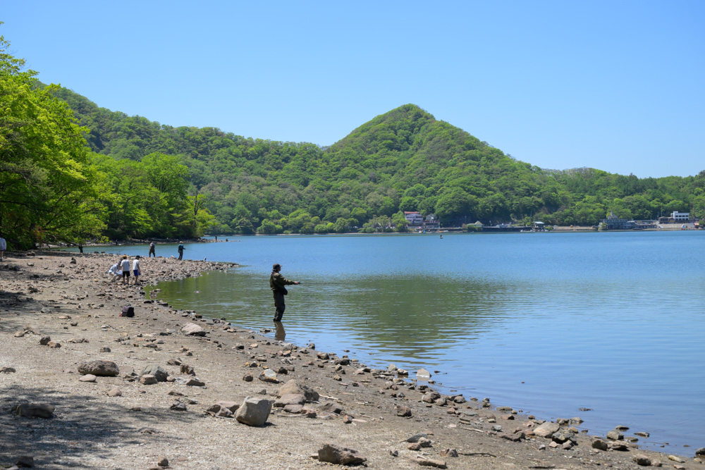 青空の下に広がる榛名湖畔の景色。澄んだ湖と新緑、爽やかな空が美しく、自然の癒しを感じられる風景。