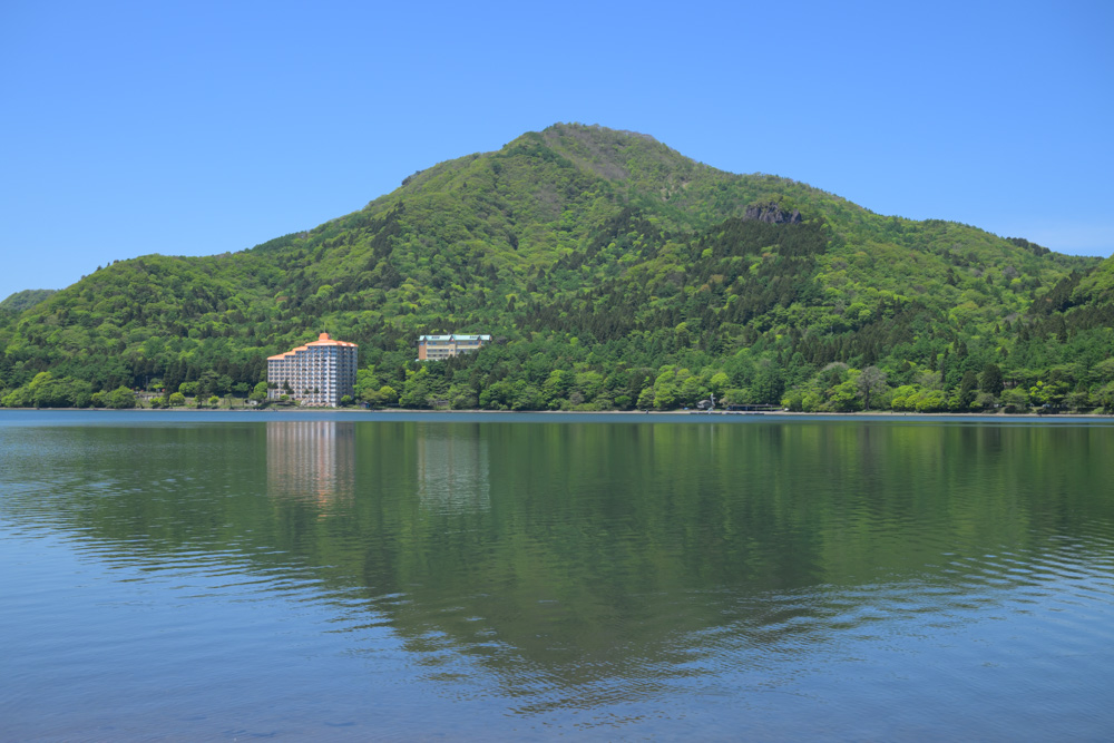 青空の下に広がる榛名湖畔の景色。澄んだ湖と新緑、爽やかな空が美しく、自然の癒しを感じられる風景。