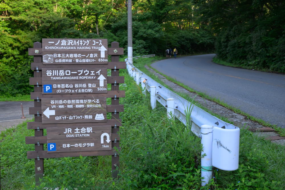 一ノ倉沢ハイキングコースや谷川岳ロープウェイ、JR土合駅への案内看板。奥には登山口へ続く道が続いている