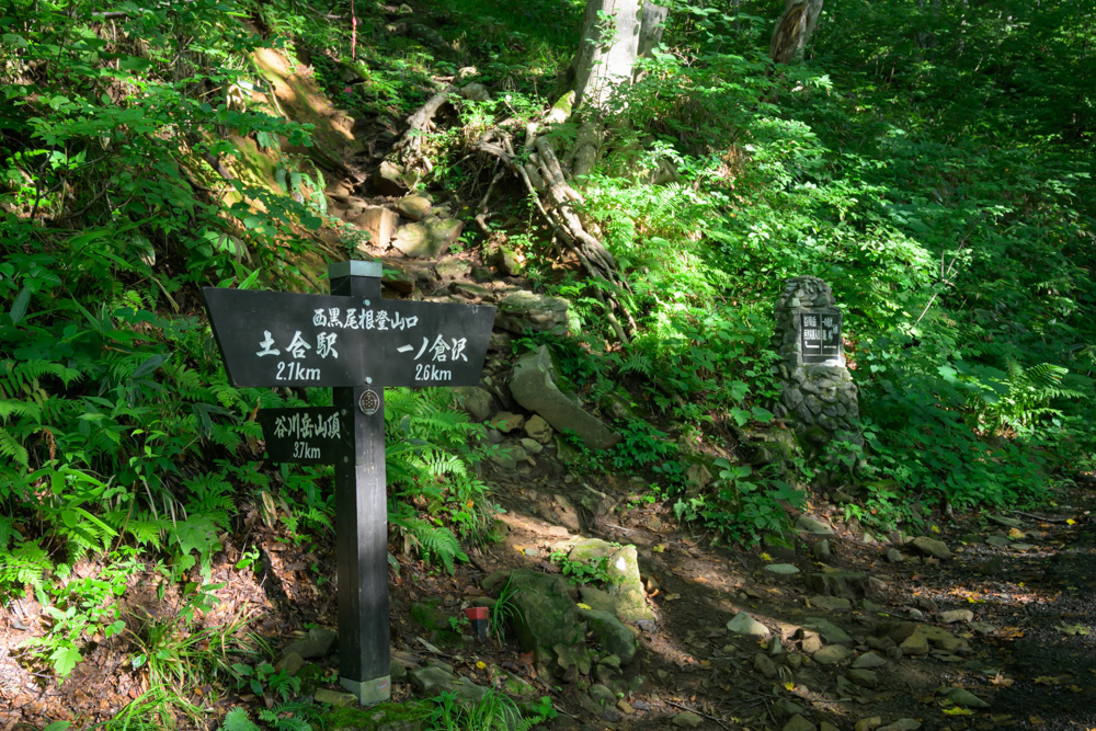 西黒尾根登山口の道標。谷川岳山頂まで3.7kmと表示され、岩の多い登山道が奥に続いている