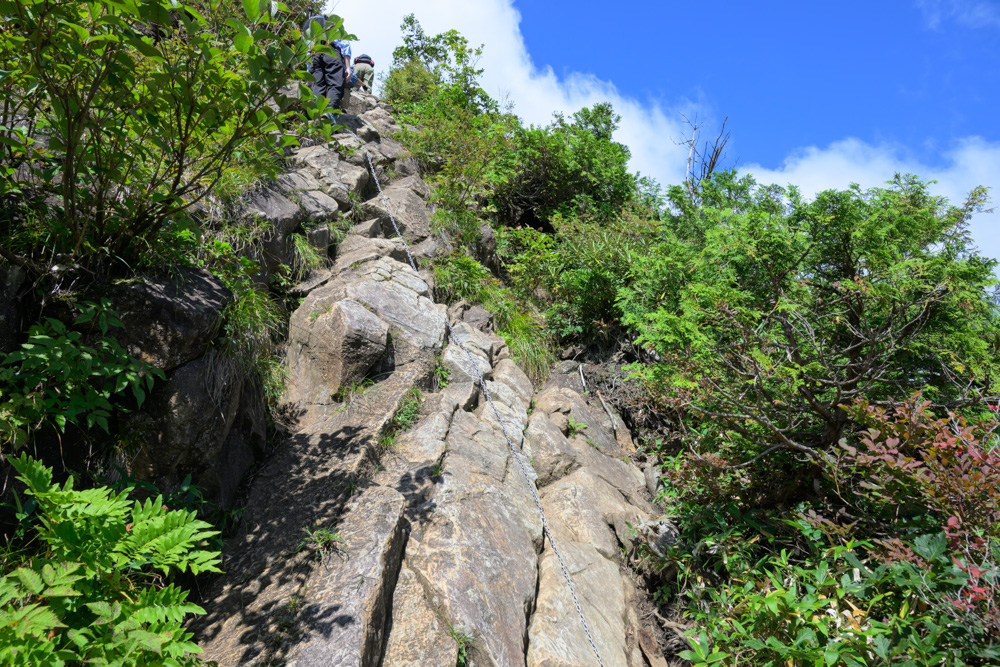 西黒尾根の鎖場。急な岩壁に鎖が張られ、登山者が上部を登っている