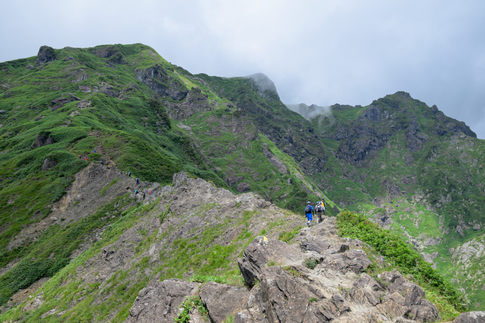 西黒尾根の稜線を歩く登山者たち。奥の山には雲がかかっている