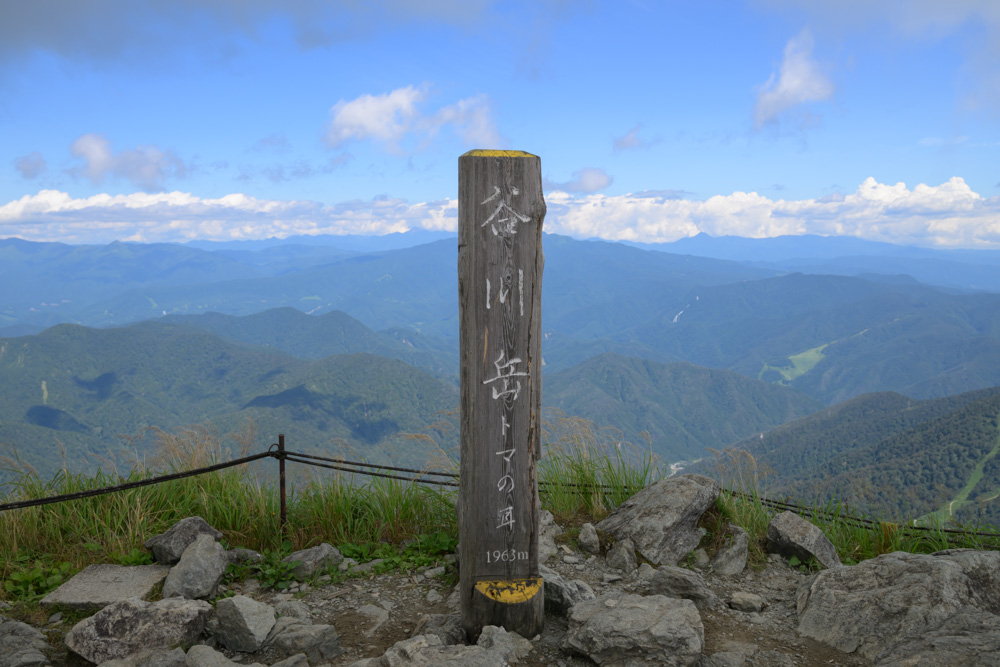 谷川岳トマノ耳の山頂標識。標高1963mと表示され、山々の眺望が広がっている