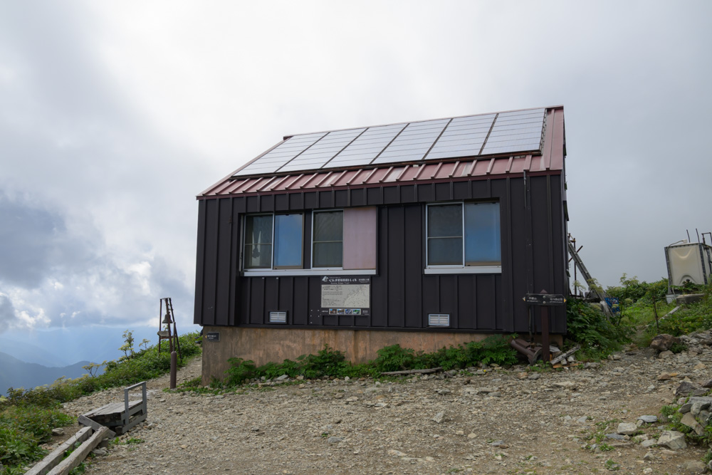 谷川岳肩の小屋の外観。黒い外壁に赤い屋根、太陽光パネルが設置されている
