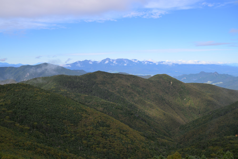 青空の下に重なる山並みと、遠くに見える山々