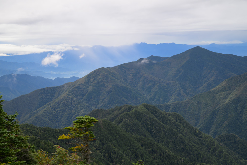 緑の山並みが幾重にも重なり、遠くに青くかすむ山々と雲が広がる景色
