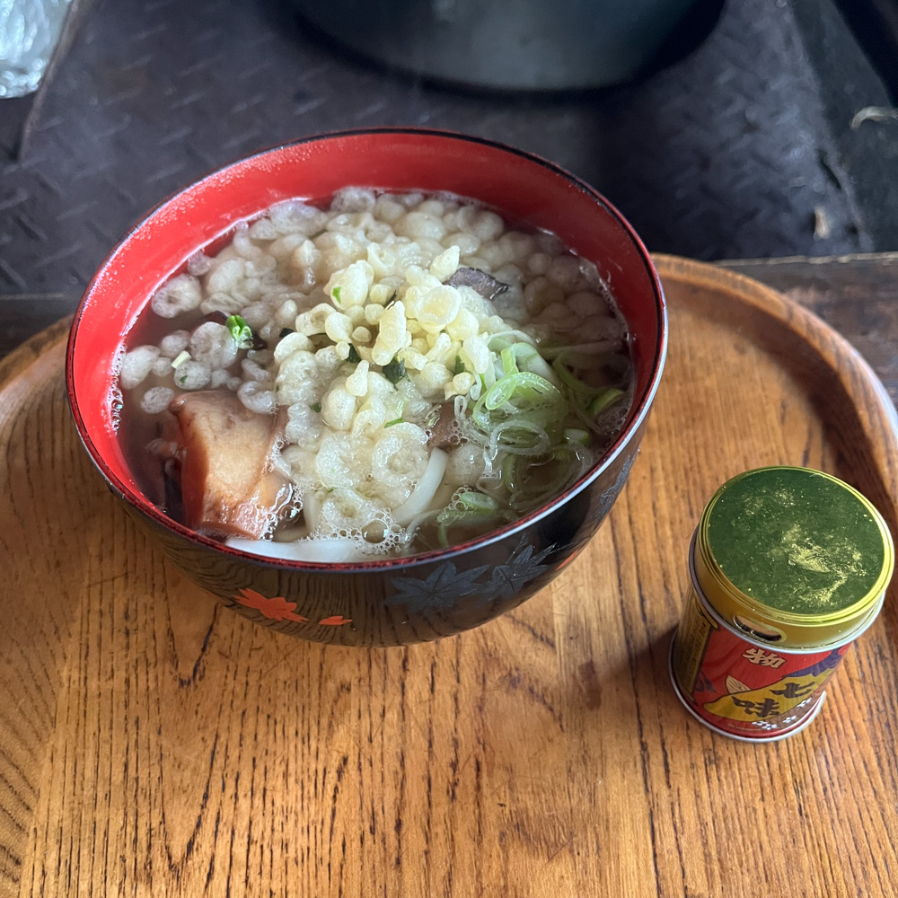 木のお盆にのった温かいきのこうどんと、七味の缶