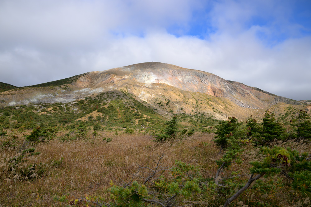 ススキの草原の奥にそびえる、山肌がむき出しになった一切経山
