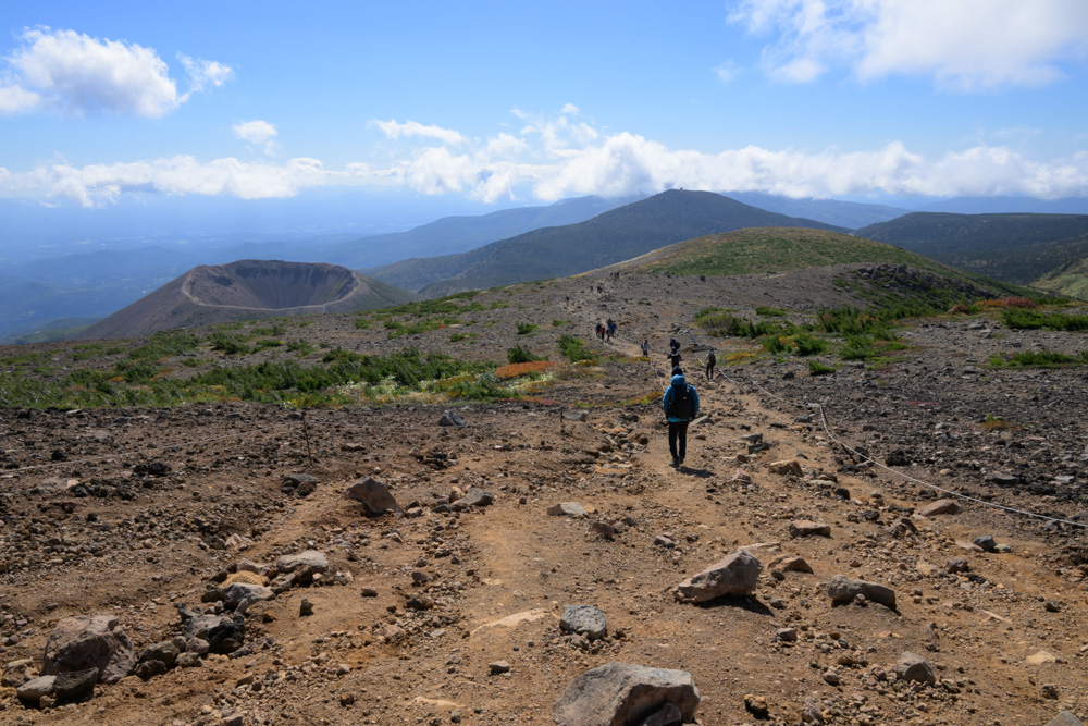 一切経山の山頂付近に広がる砂礫の道と登山者。奥に吾妻小富士の火口が見える