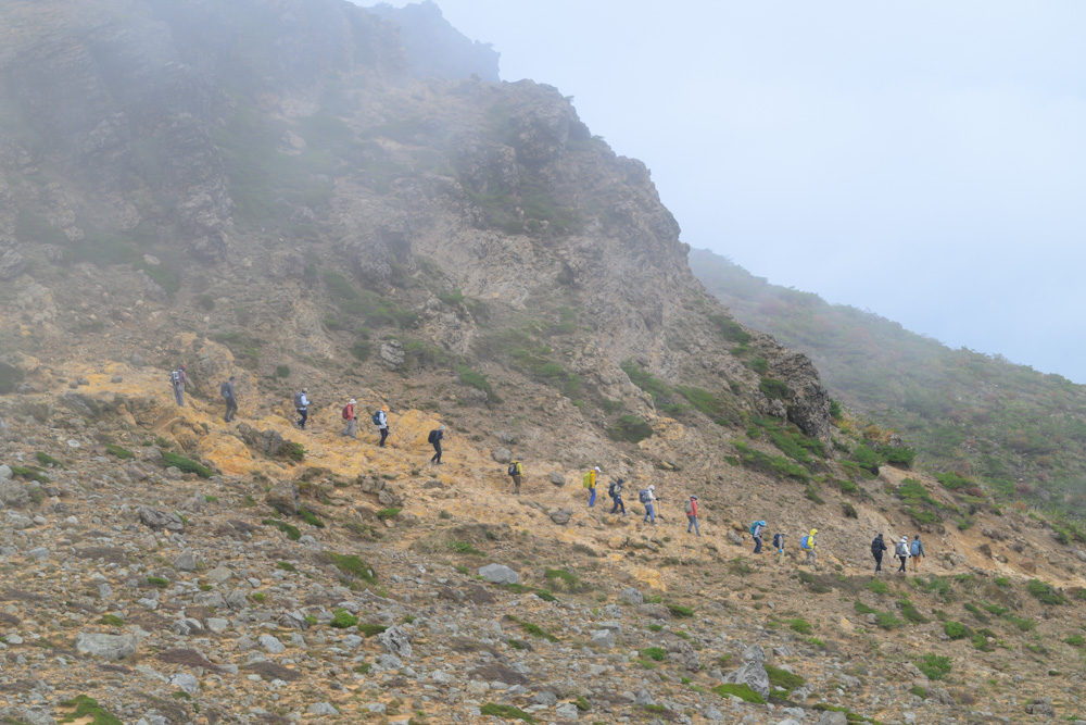 ガスが流れる斜面を一列になって歩く登山者たち
